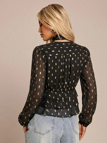 Women's black long-sleeve chiffon blouse with metallic foil dots, a V-neck, a scarf tie, and a tiered ruffled hem paired with blue jeans.