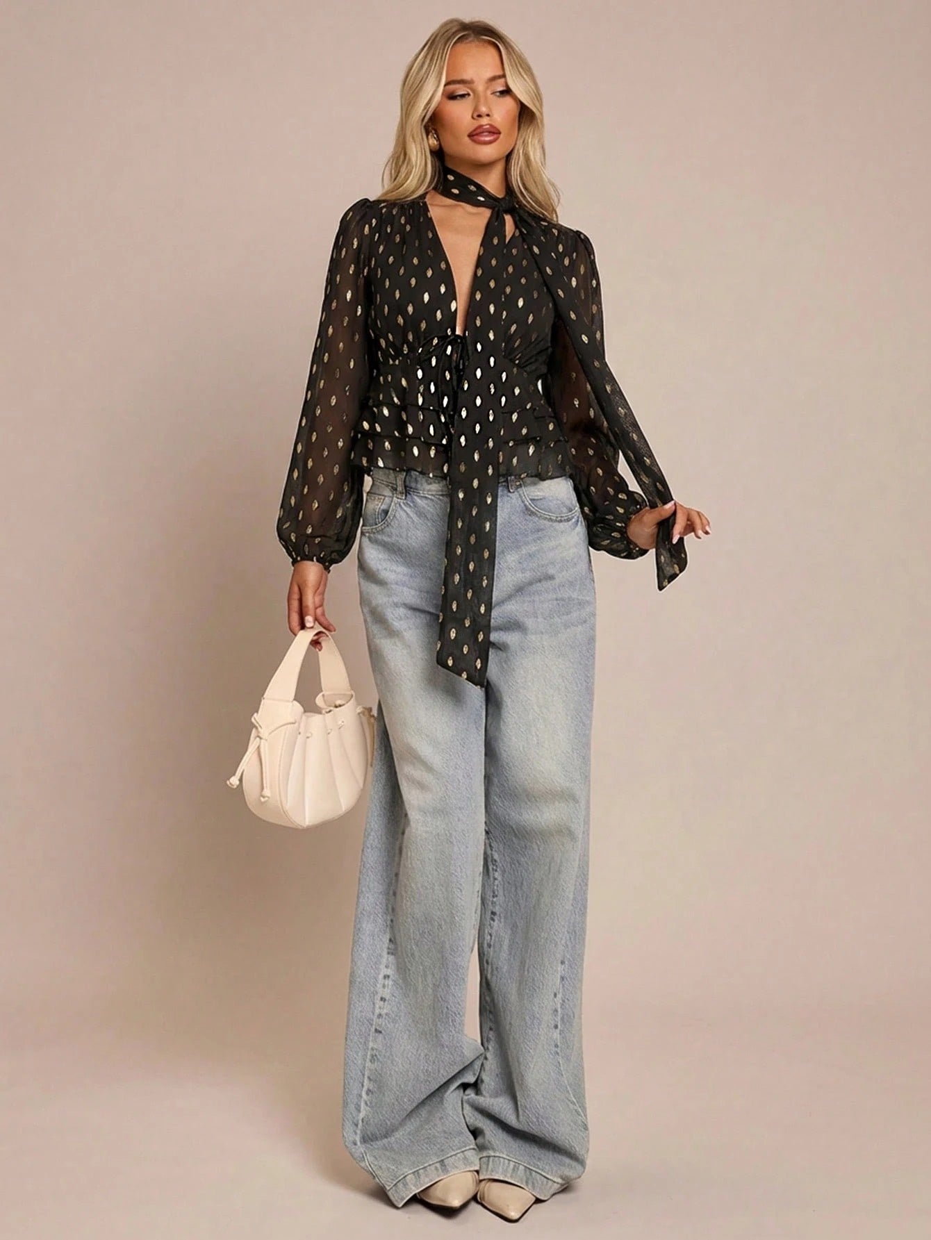 Women's black long-sleeve chiffon blouse with metallic foil dots, a V-neck, a scarf tie, and a tiered ruffled hem paired with blue jeans.