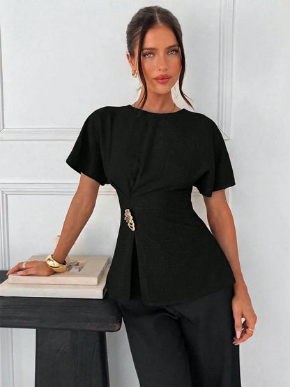 Women's black short-sleeve round neck blouse with a statement gold side waist buckle paired with black trousers for an office look.