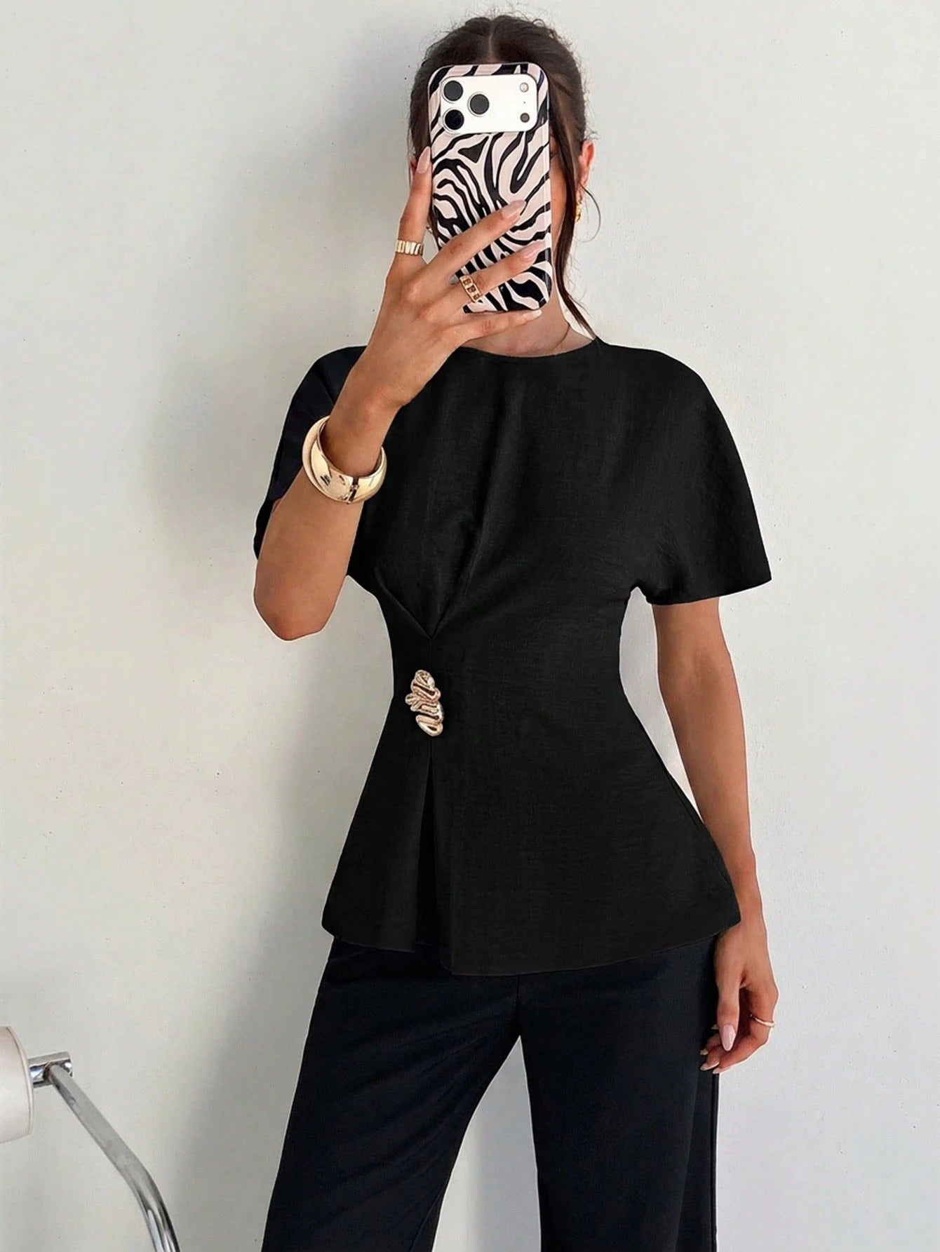 Women's black short-sleeve round neck blouse with a statement gold side waist buckle paired with black trousers for an office look.
