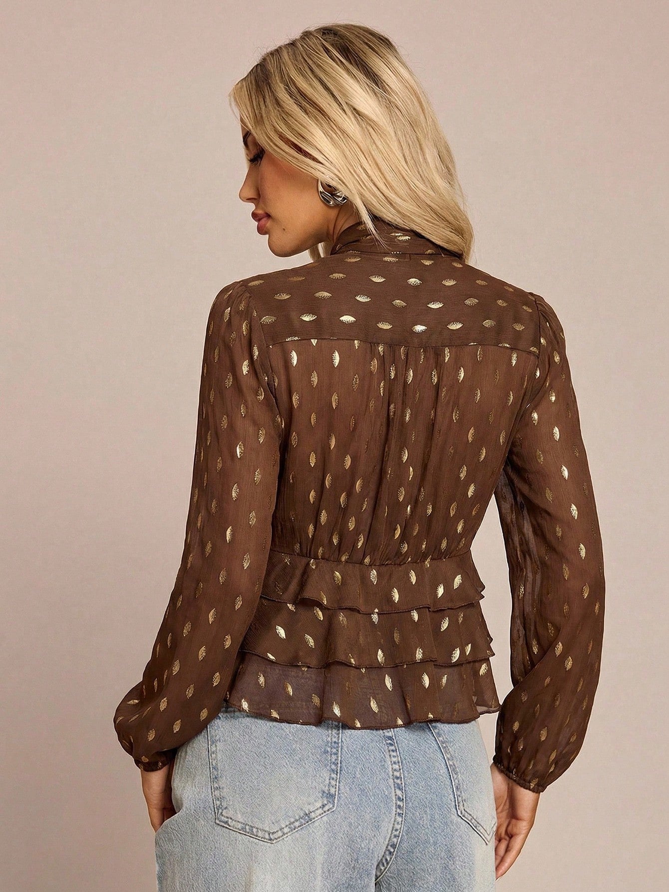 Women's brown long-sleeve chiffon blouse with metallic foil dots, a V-neck, a scarf tie, and a tiered ruffled hem paired with blue jeans.