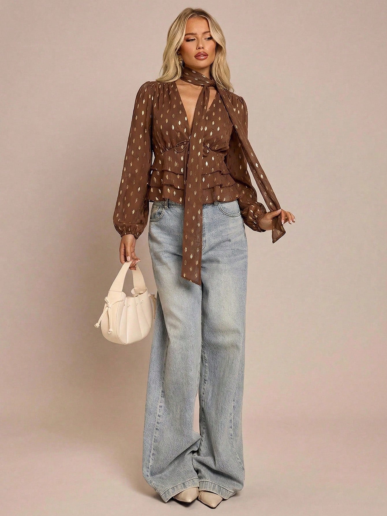 Women's brown long-sleeve chiffon blouse with metallic foil dots, a V-neck, a scarf tie, and a tiered ruffled hem paired with blue jeans.