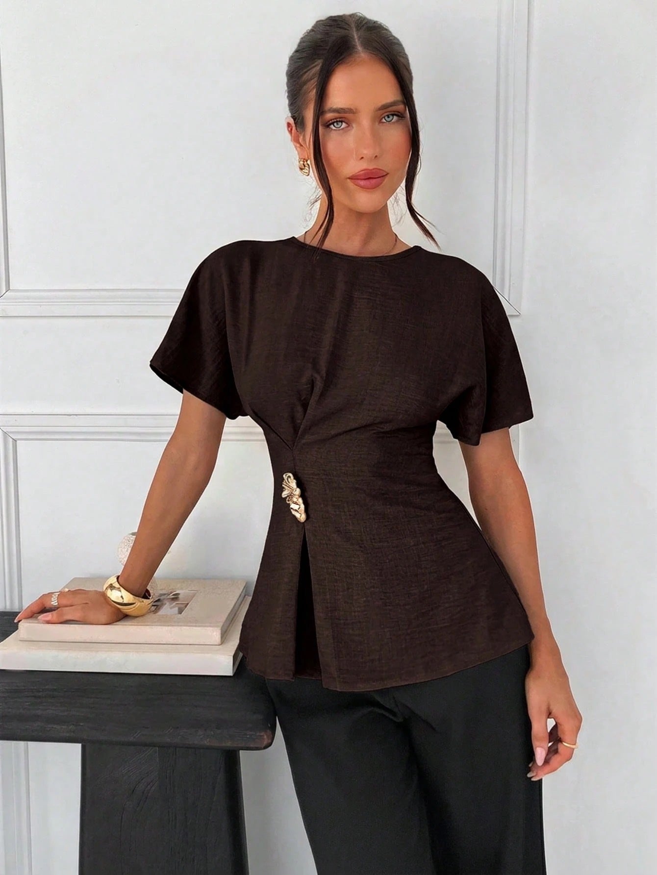 Women's brown short-sleeve round neck blouse with a statement gold side waist buckle paired with black trousers for an office look.