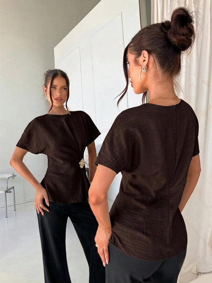 Women's brown short-sleeve round neck blouse with a statement gold side waist buckle paired with black trousers for an office look.