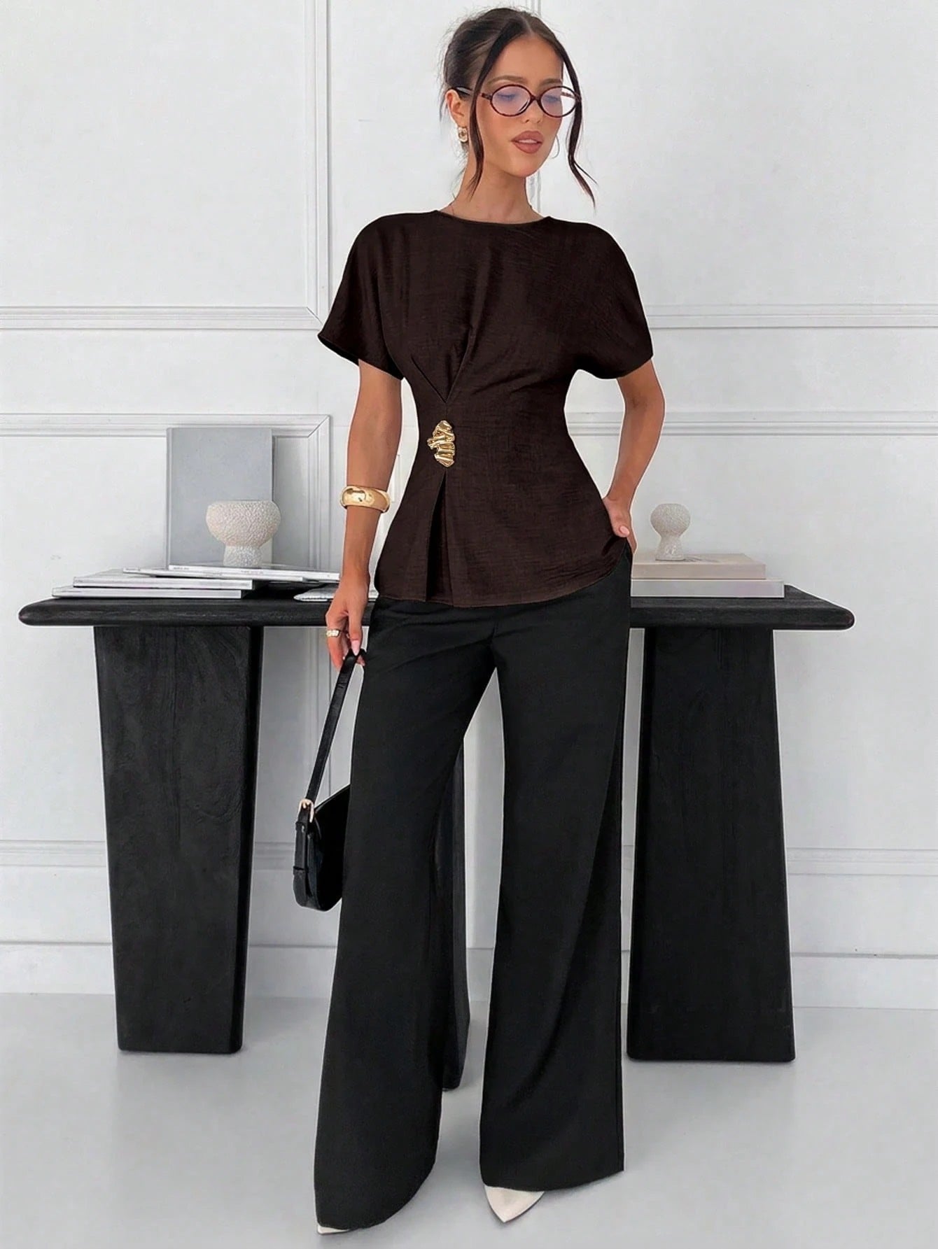 Women's brown short-sleeve round neck blouse with a statement gold side waist buckle paired with black trousers for an office look.
