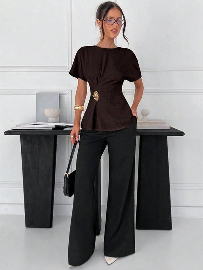 Women's brown short-sleeve round neck blouse with a statement gold side waist buckle paired with black trousers for an office look.
