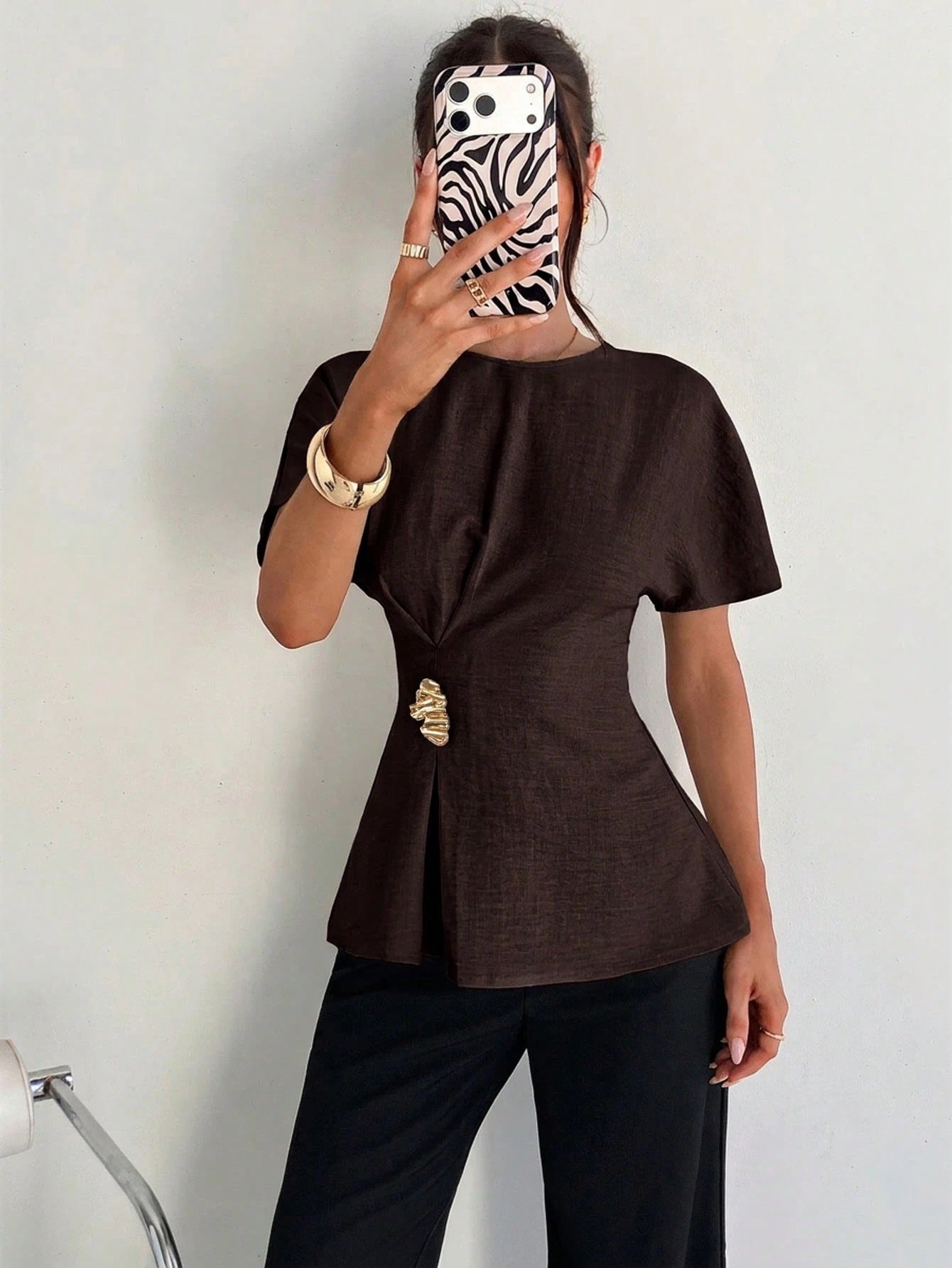Women's brown short-sleeve round neck blouse with a statement gold side waist buckle paired with black trousers for an office look.