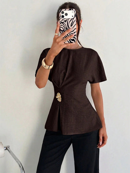 Women's brown short-sleeve round neck blouse with a statement gold side waist buckle paired with black trousers for an office look.