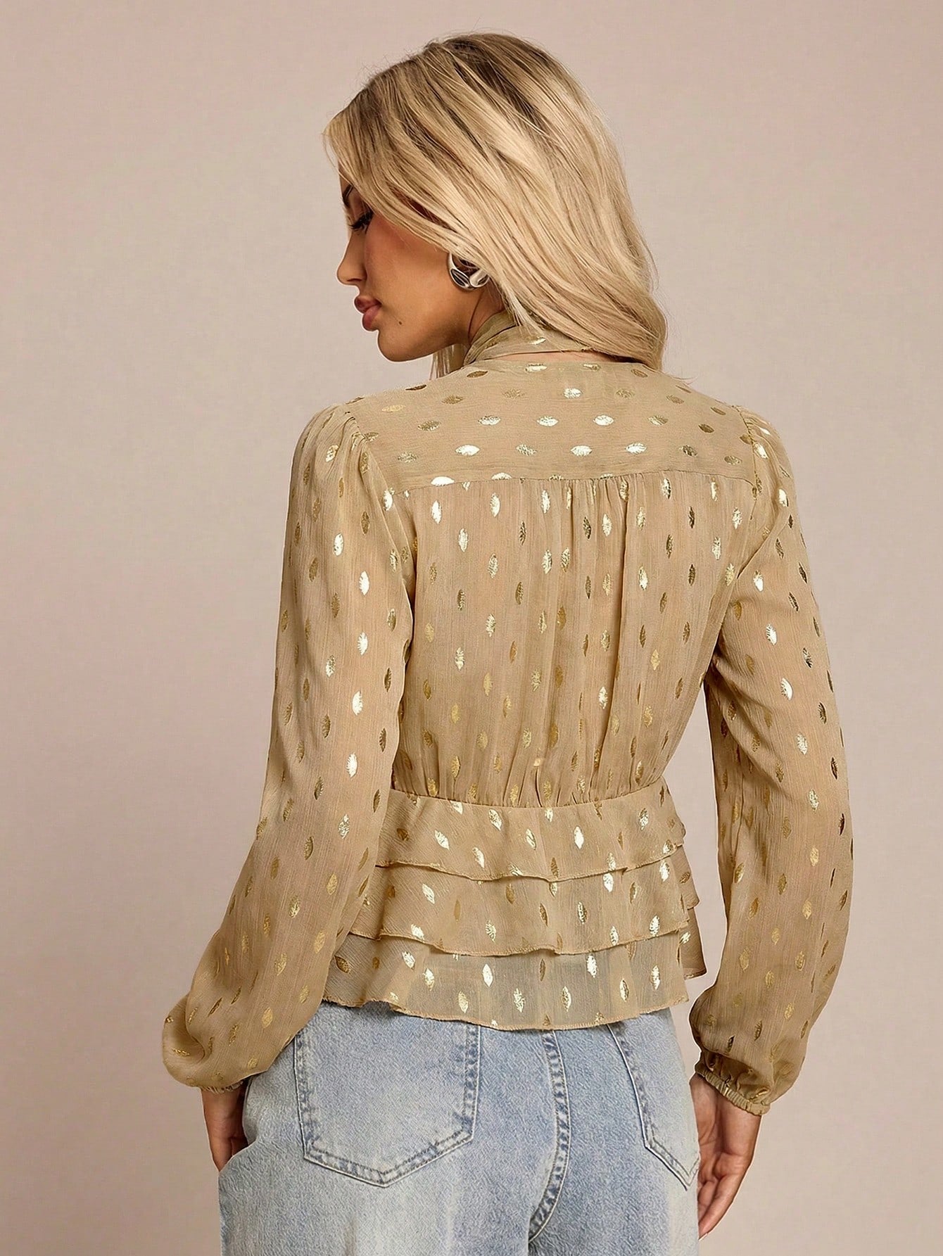 Women's khaki long-sleeve chiffon blouse with metallic foil dots, a V-neck, a scarf tie, and a tiered ruffled hem paired with blue jeans.