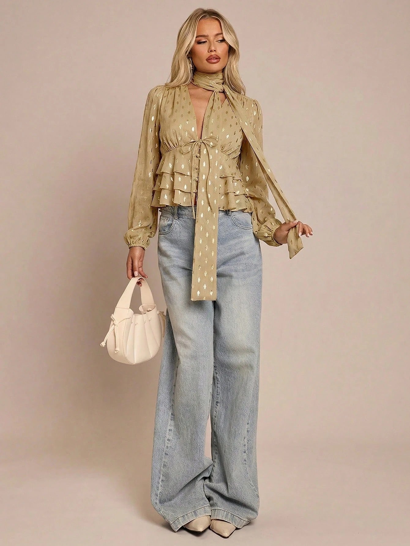 Women's khaki long-sleeve chiffon blouse with metallic foil dots, a V-neck, a scarf tie, and a tiered ruffled hem paired with blue jeans.