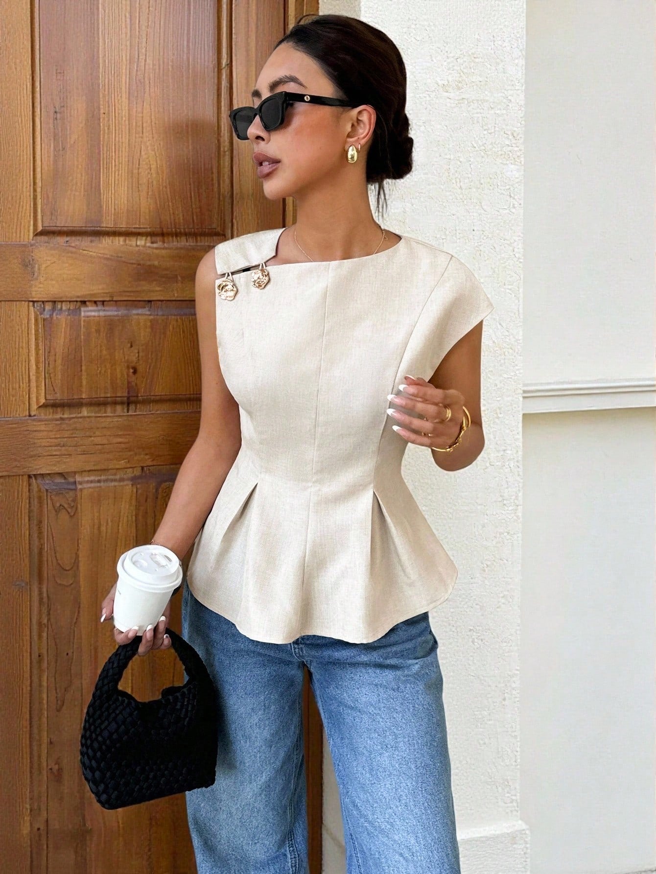 Women's minimalist apricot sleeveless peplum blouse with gold button accents and a pleated flare hem paired with blue jeans.