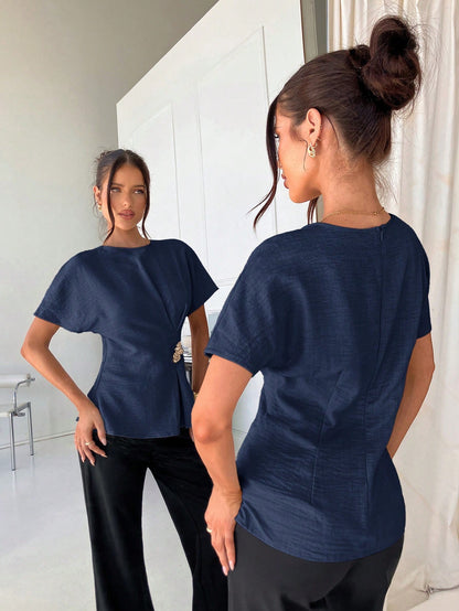Women's navy blue short-sleeve round neck blouse with a statement gold side waist buckle paired with black trousers for an office look.