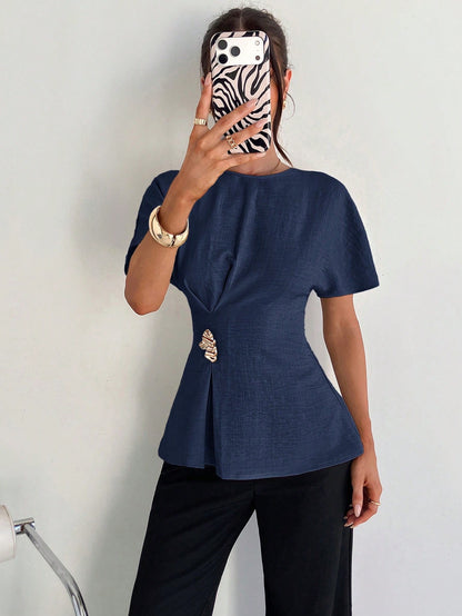 Women's navy blue short-sleeve round neck blouse with a statement gold side waist buckle paired with black trousers for an office look.