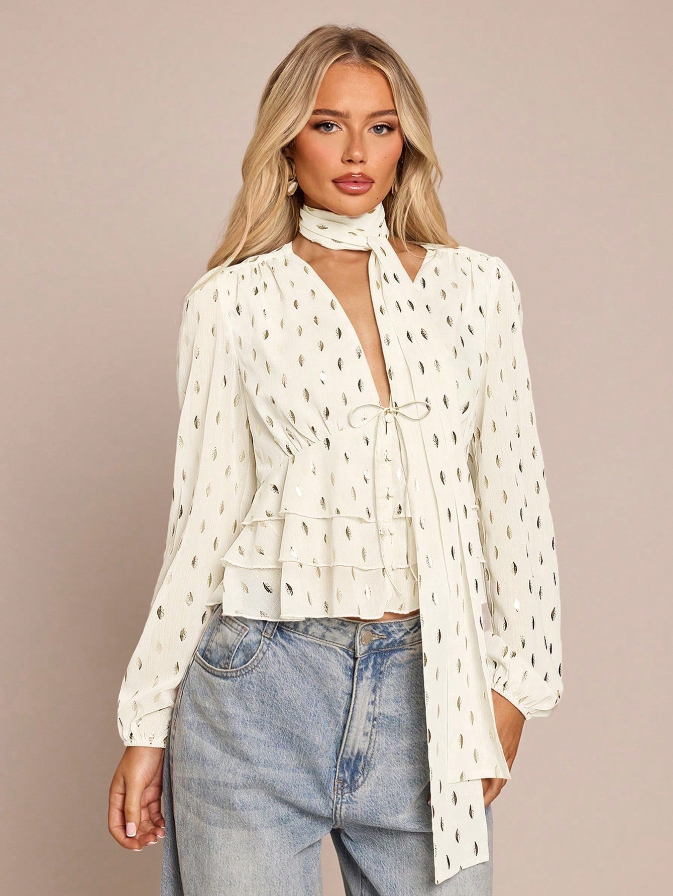 Women's white long-sleeve chiffon blouse with metallic foil dots, a V-neck, a scarf tie, and a tiered ruffled hem paired with blue jeans.