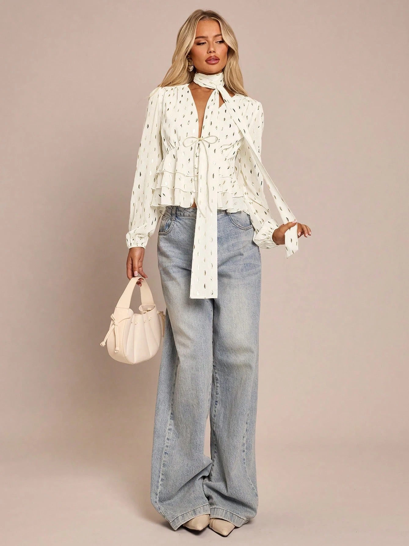 Women's white long-sleeve chiffon blouse with metallic foil dots, a V-neck, a scarf tie, and a tiered ruffled hem paired with blue jeans.