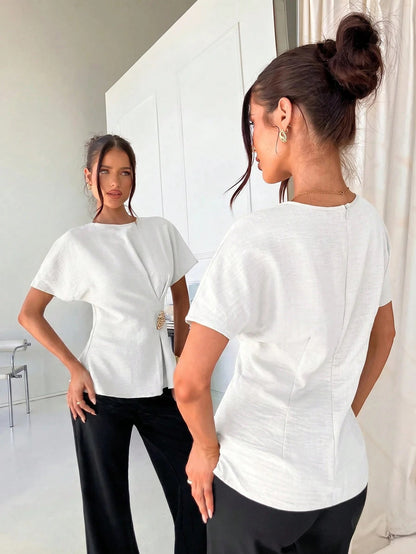 Women's white short-sleeve round neck blouse with a statement gold side waist buckle paired with black trousers for an office look.1