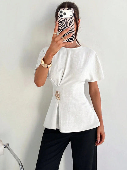 Women's white short-sleeve round neck blouse with a statement gold side waist buckle paired with black trousers for an office look.
