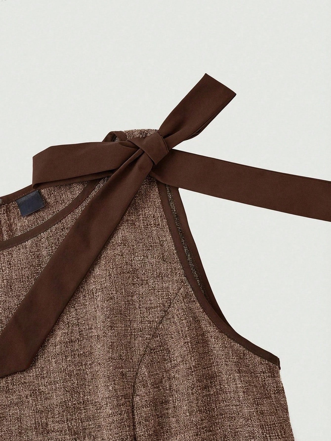 brown wide-leg sleeveless jumpsuit featuring contrast brown shoulder bow ties and trim laid flat against a neutral background