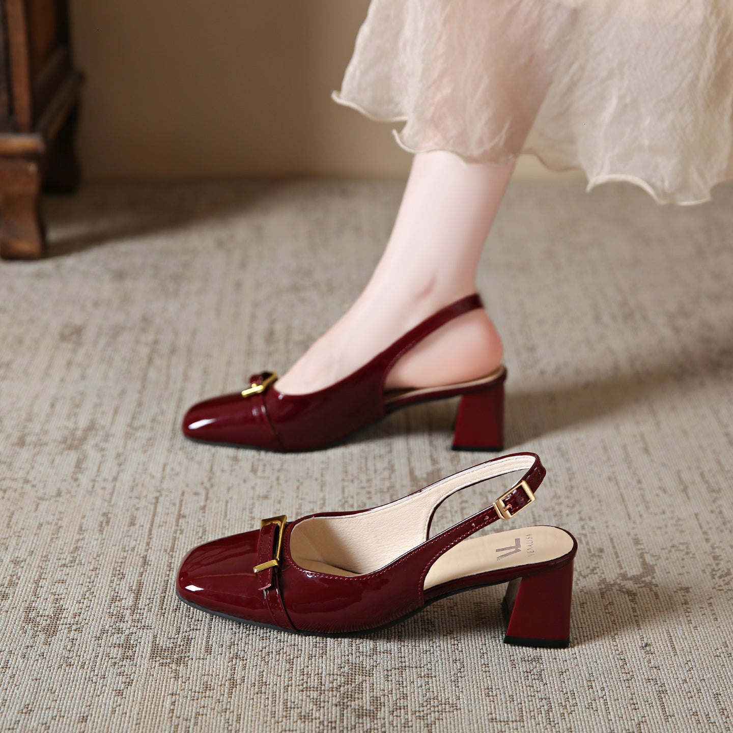 Red high-heeled shoes with gold buckles worn by a person on a textured floor.