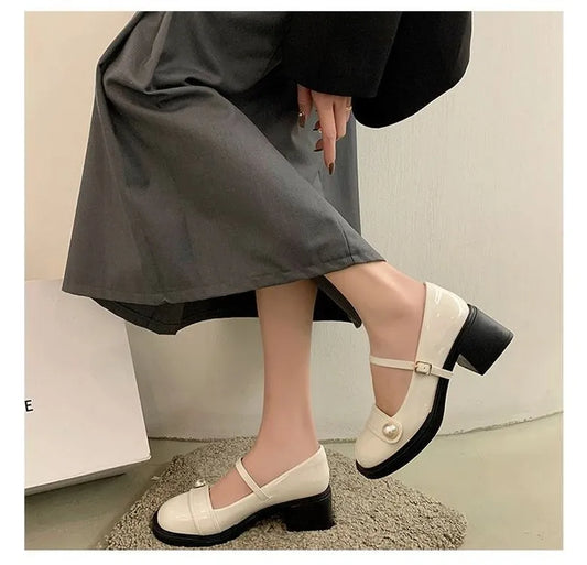 White shoes with black soles worn by a person in a gray skirt and black coat.